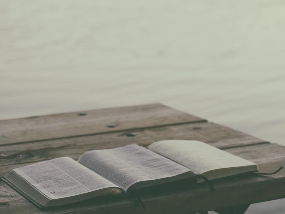 Open Bible on a wooden table by calm water – Bible verses to pray against witchcraft