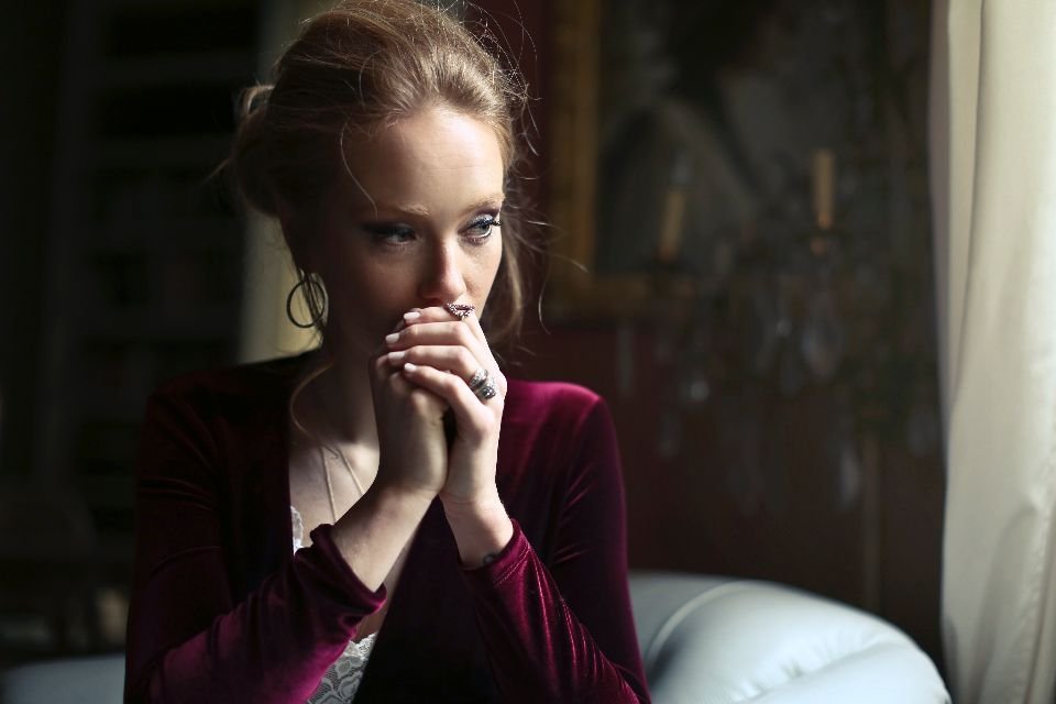 Woman clasping her hands in prayer by a window – breaking generational curses through faith in Jesus