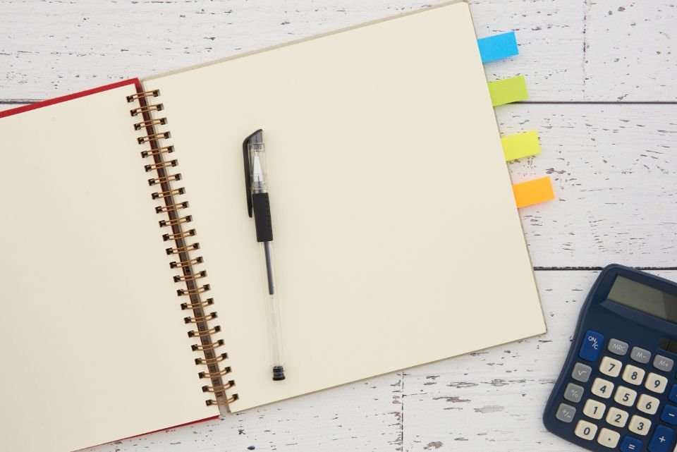 An open notebook, pen and calculator on a white desk – writing a simple budget alongside prayer for provision