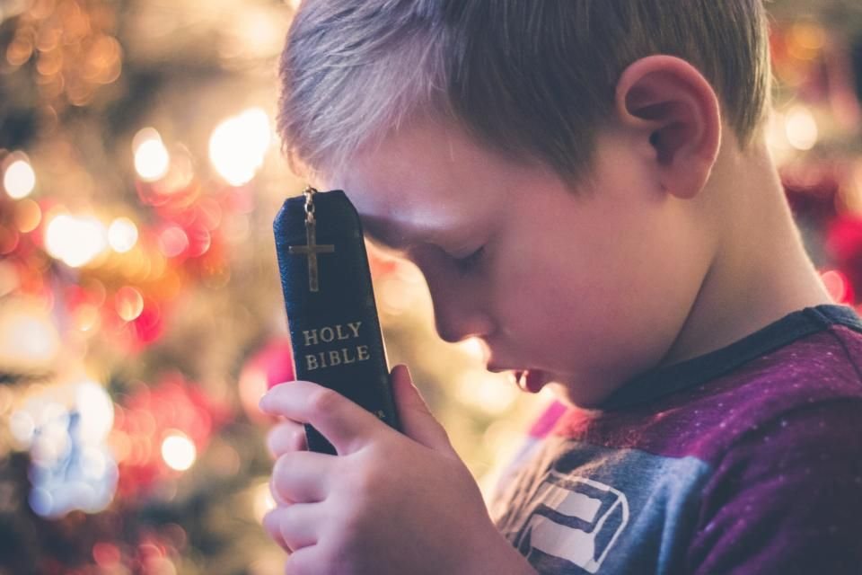 Young child resting forehead on a Holy Bible in prayer – a new generation walking free in Christ