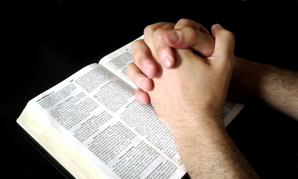 Hands folded in prayer on an open Bible – a couple seeking God’s help in their relationship