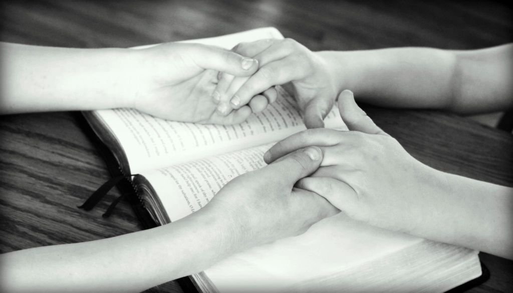 A husband and wife holding hands in prayer over an open Bible – praying for restoration of marriage