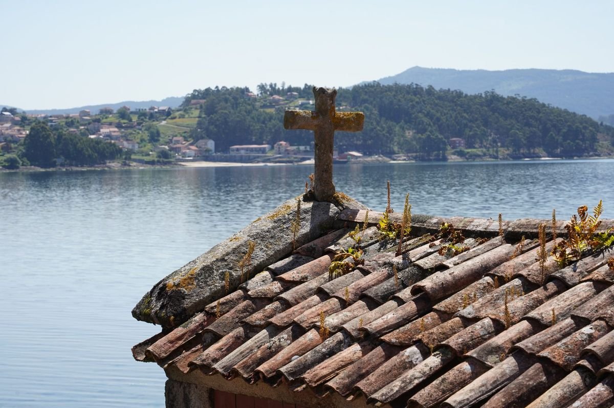 A stone cross on a rooftop overlooking calm water and hills – Christ’s authority over the waters