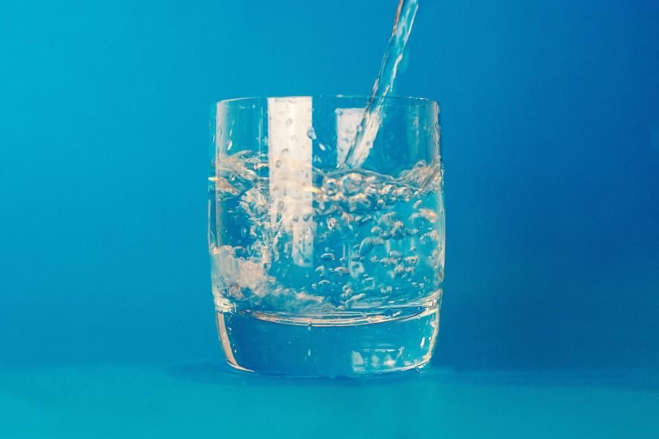 Glass of clear water on a blue background – drink water and fast safely