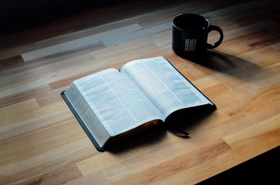 Open Bible and coffee mug on a wooden table – reading Esther and praying Esther fast prayer points
