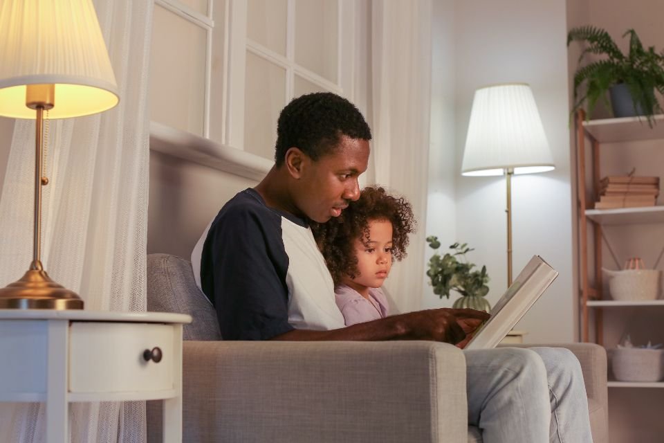 A father reading with his young daughter in a warmly lit living room – praying for protection over your family and home