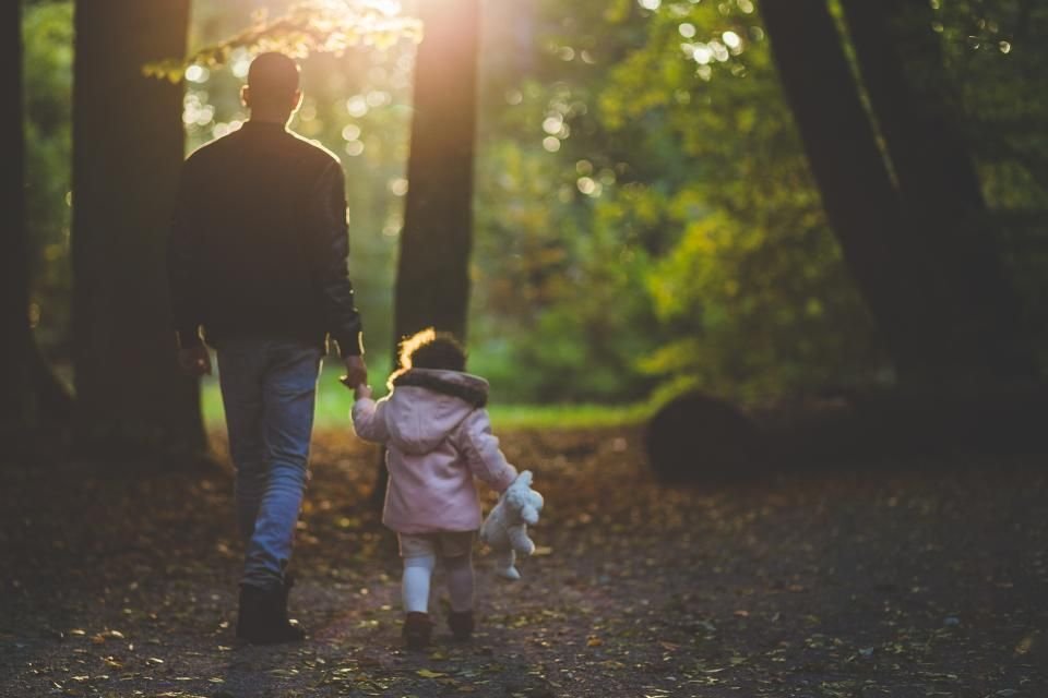 Father holding his young daughter’s hand on a sunlit path – protecting and caring for children