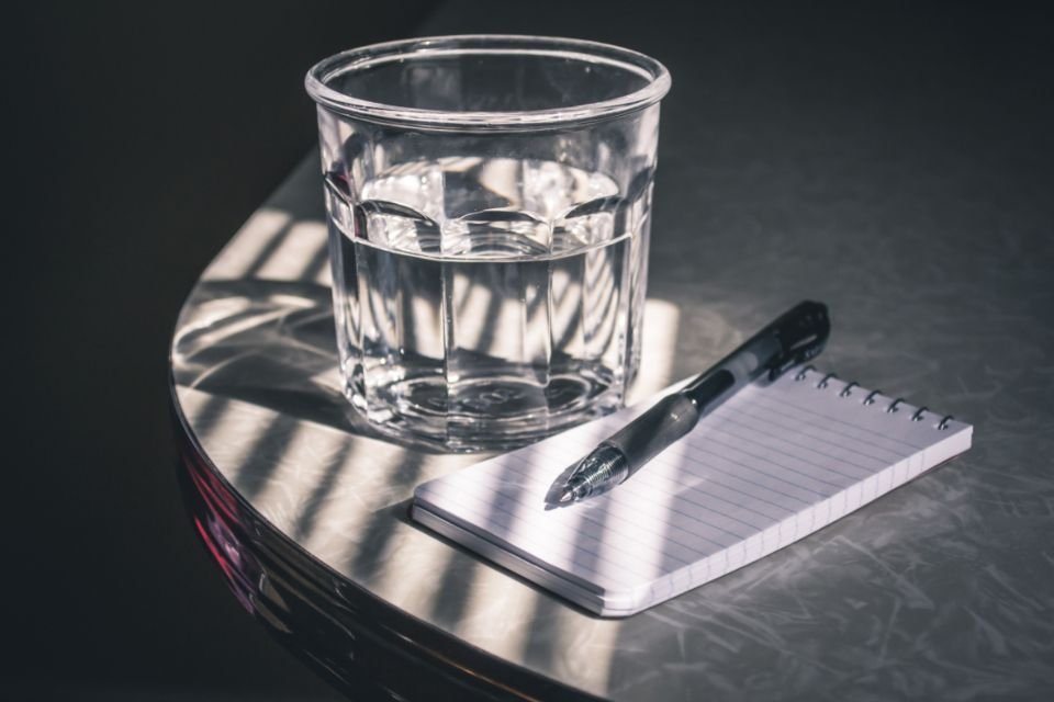 A glass of water beside a notebook and pen – keep drinking water and write down your prayer requests during a 3-day fast