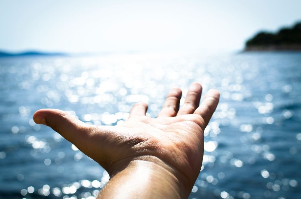 Open hand reaching toward sunlit water – letting go of the past to break soul ties in Christ