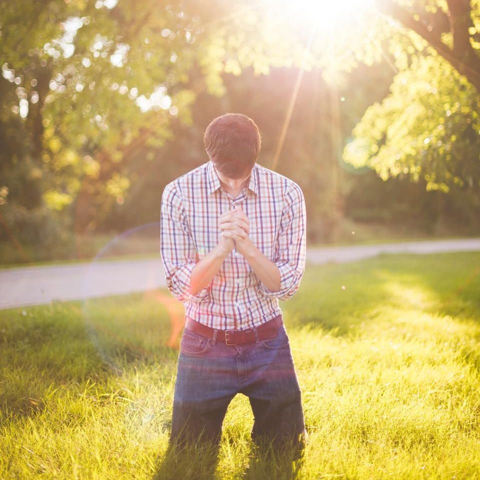 Young man with head bowed praying in a sunlit field – praying for freedom from a spiritual wife in Jesus’ name