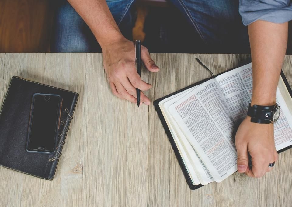 Man writing prayer points in a notebook beside an open Bible – praying Scripture against a spiritual wife