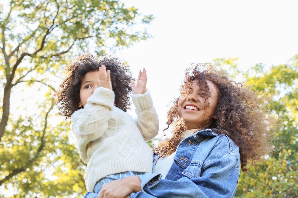 A smiling mother holding her young daughter outdoors in the sunshine – a blessing over children as they grow
