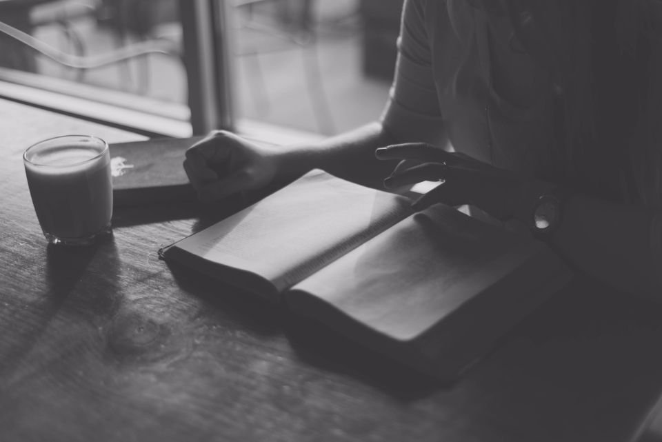 An open book and a glass on a wooden table – setting aside quiet time to read Scripture and pray for deliverance