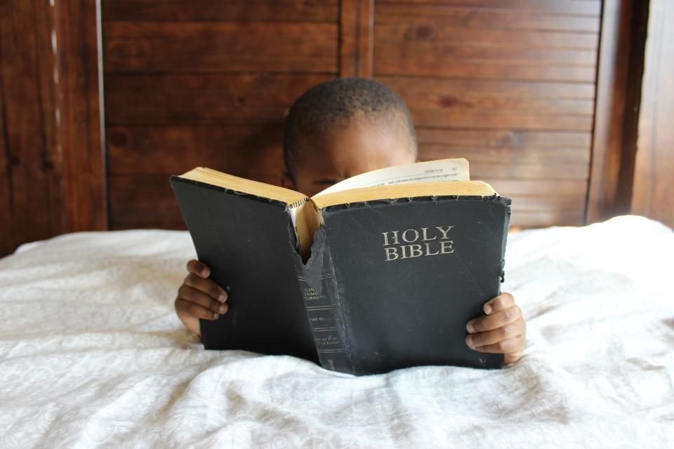 Child reading a Holy Bible in bed at bedtime – prayer against bad dreams for children