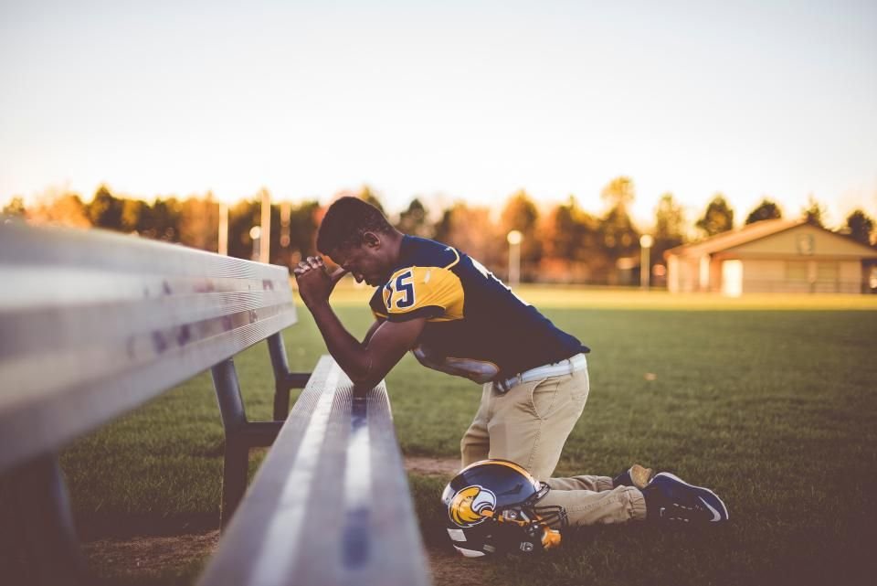 Young man kneeling in prayer at sunset beside a bench – prayer against spiritual wife in the name of Jesus