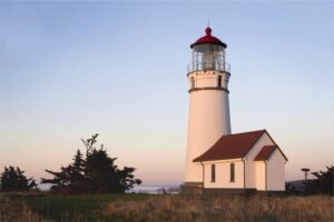 A white lighthouse standing firm at sunset beside a small house – a picture of God's protection against evil
