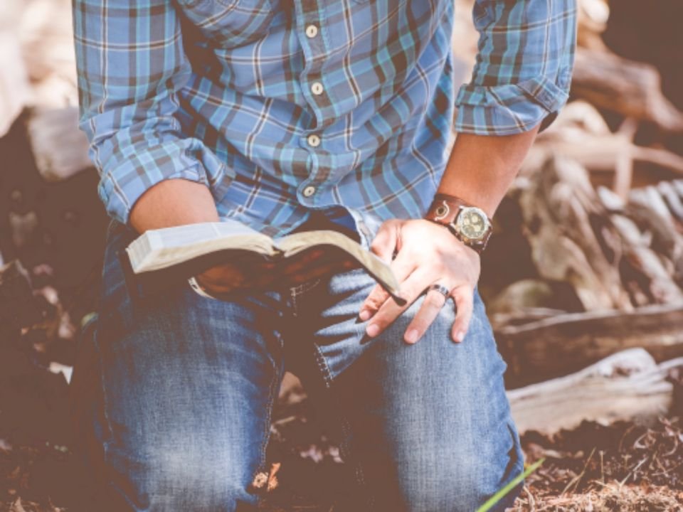 Man kneeling outdoors with an open Bible – a Christian man seeking God about signs of spiritual wife