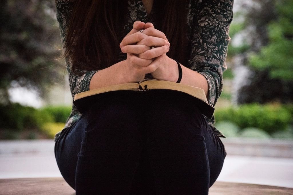 Woman with hands clasped in prayer over an open Bible – praying about spiritual husband and children