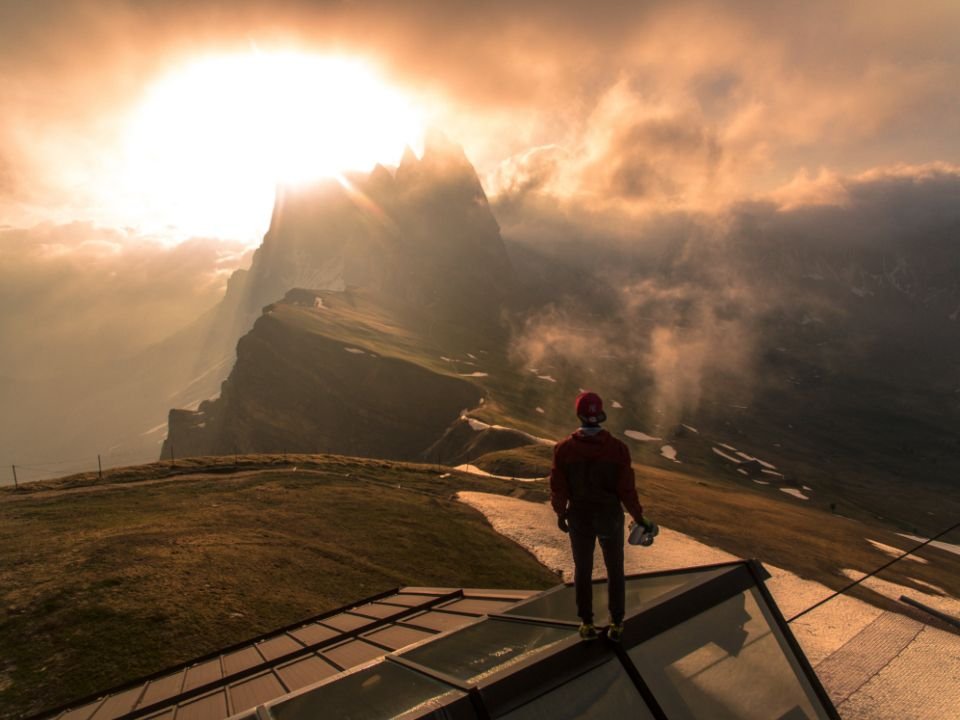 A person standing on a mountain viewpoint as the sun breaks through the clouds – walking in the freedom Christ has won
